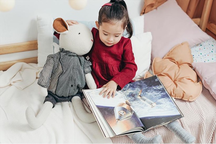 A little girl reading a book to her stuffed animal