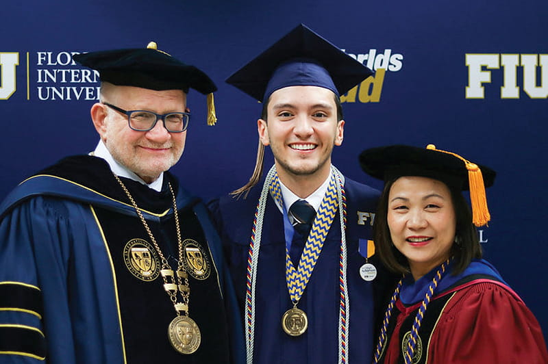 President Mark B. Rosenberg and Dean Joanne Li at fall 2019 commencement with Julio Leon Penate, who served as the banner marshal representing his graduating class.