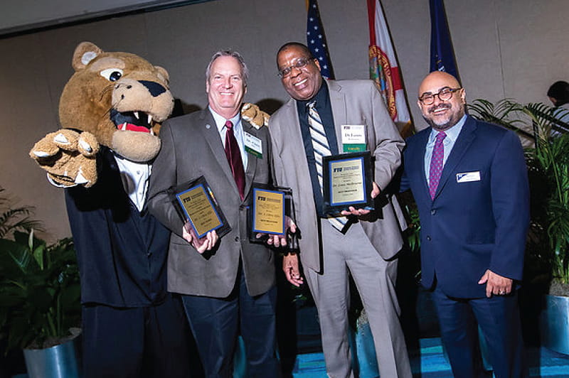 Roary, FIU's mascot, Steven Ellis, instructor, information systems and business analytics, Louis Melbourne, senior instructor, information systems and business analytics, and Angel Burgos, executive director, MBA programs, at the fall 2019 MIB and MBA graduation dinner.