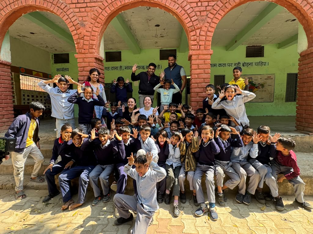 Children at a school near Bandhwari Village making playful faces with FIU visitors under a brick archway